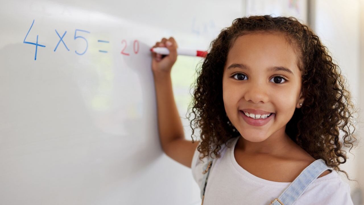 Image of a young girl doing a math problem on a whiteboard