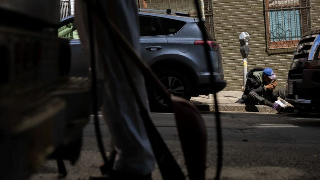Image of a man sitting on a sidewalk lighting a crackpipe