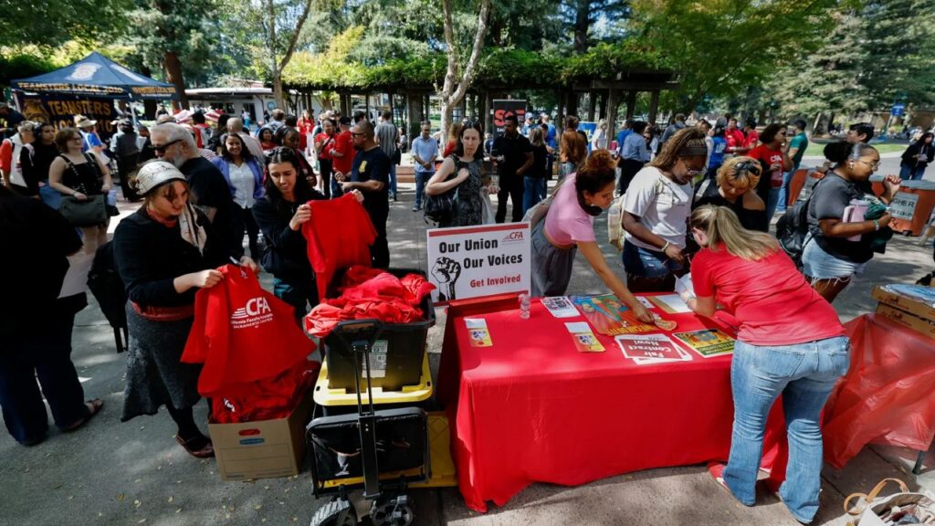 Image of people at a union rally coming up to a table to get information. Organizers are wearing red shirts