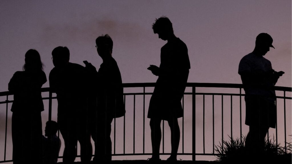 FILE PHOTO: People use their mobile phones, ahead of new law banning social media for users under 16 in Australia, at dusk in Brisbane, Australia, December 8, 2025. Reuters/Hollie Adams/File Photo