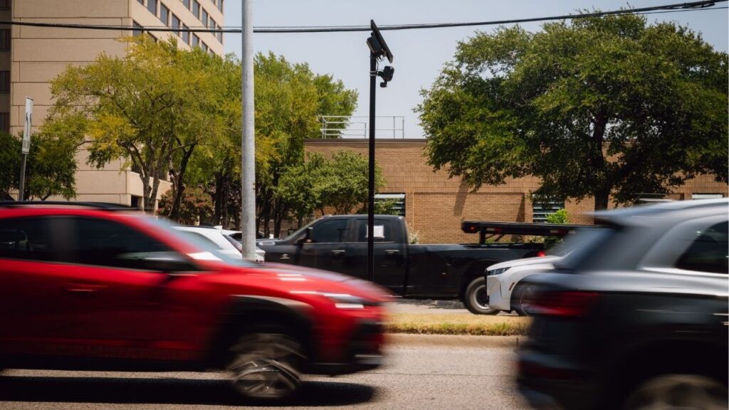 Traffic passes a Flock camera, which records license plates, atop a pole on a median in Farmers Branch, Texas, Aug. 3, 2026. Last week, Texas Gov. Greg Abbott directed police departments to stop spending state money on Flock Safety cameras, the license-plate readers that have drawn bipartisan backlash around the country, and days later Florida Gov. Ron DeSantis’s administration ordered the systems removed from state roads. (Desiree Rios/The New York Times)