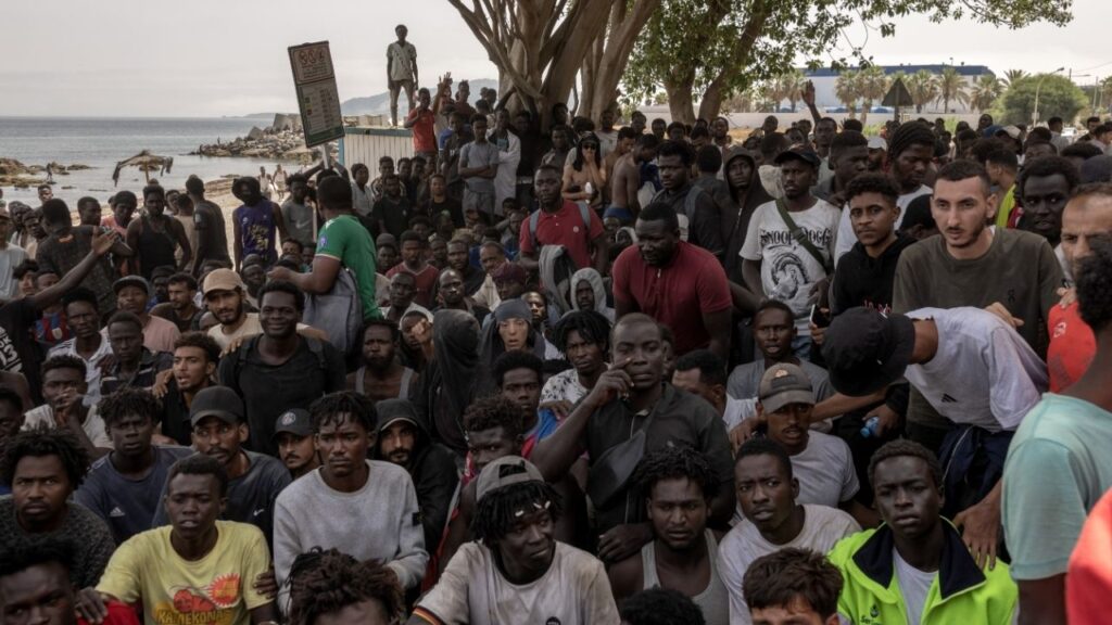 Men, many from sub-Saharan Africa, wait on a beach for humanitarian assistance in Ceuta, Spain, after crossing from Morocco into the exclave on the Mediterranean coast of North Africa, Aug. 1, 2026. Spain’s intelligence service had alerted Morocco about social media calls for a border exodus into Ceuta, which led to more than 100 deaths and a political crisis in Spain. (Finbarr O’Reilly/The New York Times)