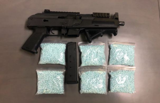 Image of a black hand rifle and packaged blue fentanyl pills
