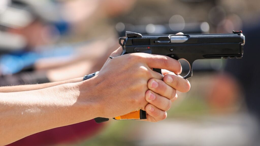 Image of a hand wrapped around the stock and trigger of a handgun facing right