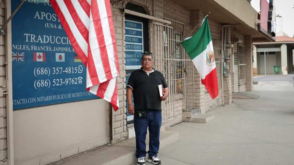 Image of a man standing on a sidewalk between US and Mexico flags