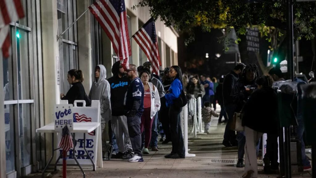 Image of voters lined up outside the downtown Fresno voting office beneath American flags