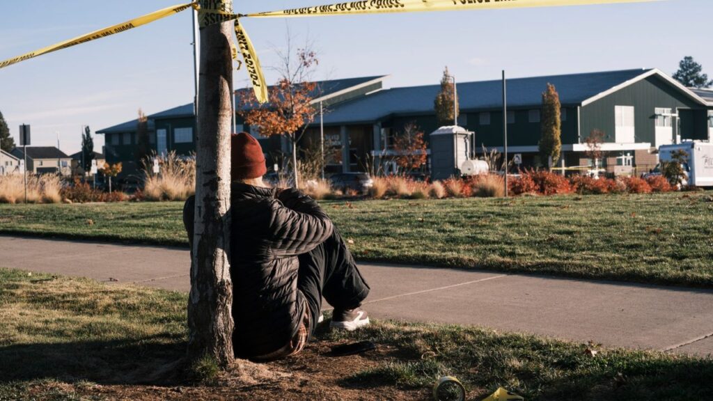 A member of the community sits at the police line outside of Silver Rail Elementary School in Bend, Ore., on Friday morning, Oct. 16, 2026. A teacher who was said to have thrown herself on top of a student during the shooting at Silver Rail Elementary School in Bend, Ore. But she wants to clear the record: She said she was given too much credit for her role. (Jordan Gale/The New York Times)