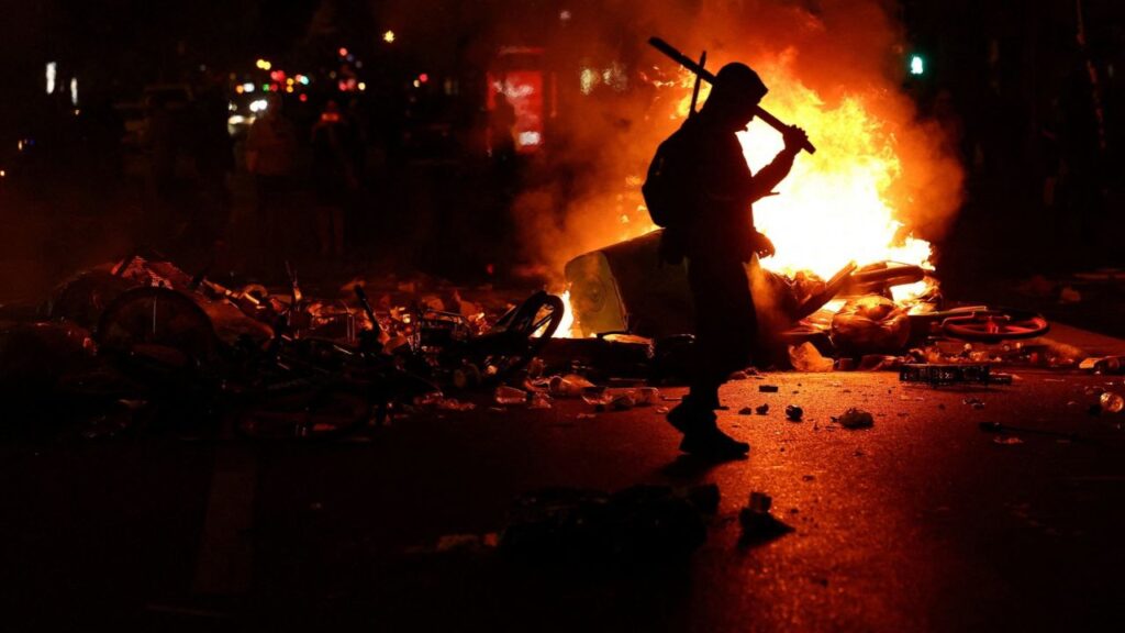 A person walks as flames rise during civil unrest, the day after a national day of demonstrations against the cost of living and rising fuel prices, in Paris, France, October 18, 2026. REUTERS/Abdul Saboor