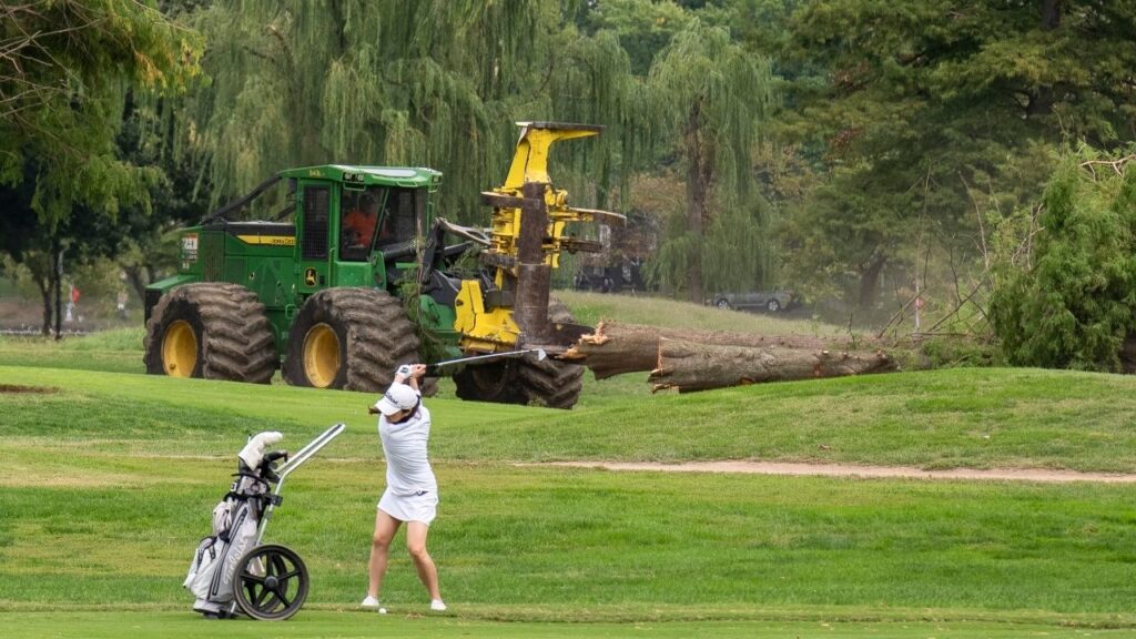 A worker moves cut-down trees as a golfer hits a shot at the East Potomac Golf Course in Washington, Oct. 10, 2026. The Trump administration will close most of East Potomac Park in Washington beginning on Nov. 15, embracing President Trump’s plan to redevelop the municipal golf course there into a championship-level course geared toward professional golfers, the government said in a court filing on Wednesday, Oct. 28, 2026. (Andrew Leyden/The New York Times)