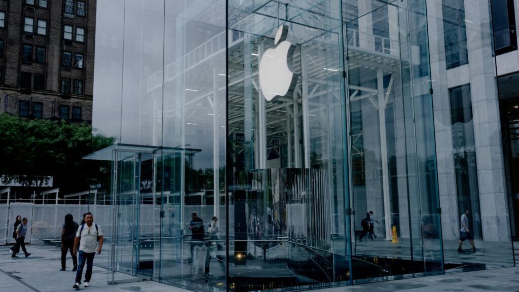 Image of an Apple store with clear windows from floor to ceilings and people passing by it