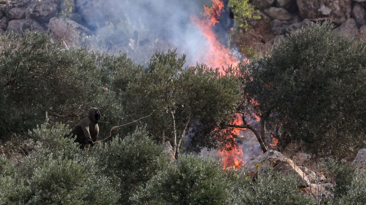 An Israeli settler casts a projectile towards Palestinians, near a fire, amid clashes during Palestinians' olive harvest in Abu Falah near Ramallah in the Israeli-occupied West Bank, October 16, 2026. REUTERS/Ammar Awad
