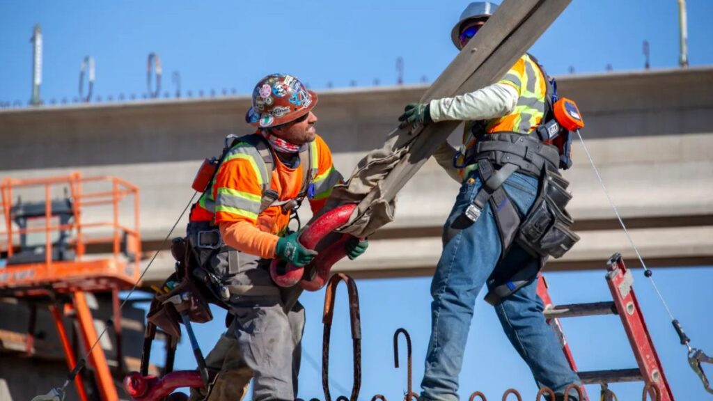Image of two construction workers handling a large object for a high-speed rail overpass in Fresno County