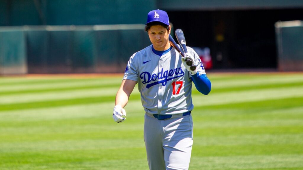 Image of Shohei Ohtani walking across a baseball field with two bats slung over his shoulder