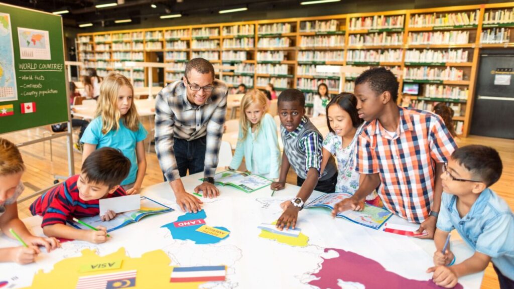 A teacher working at a table with a group of diverse, happy, young students